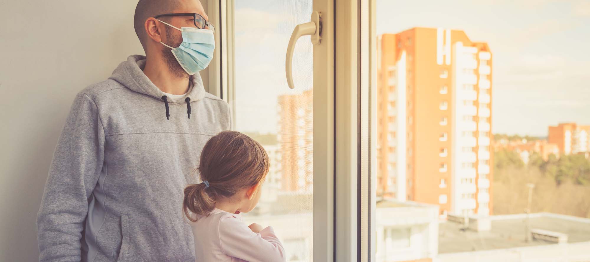 Man wearing mask while in a track suit with a child next to him both looking out of a window