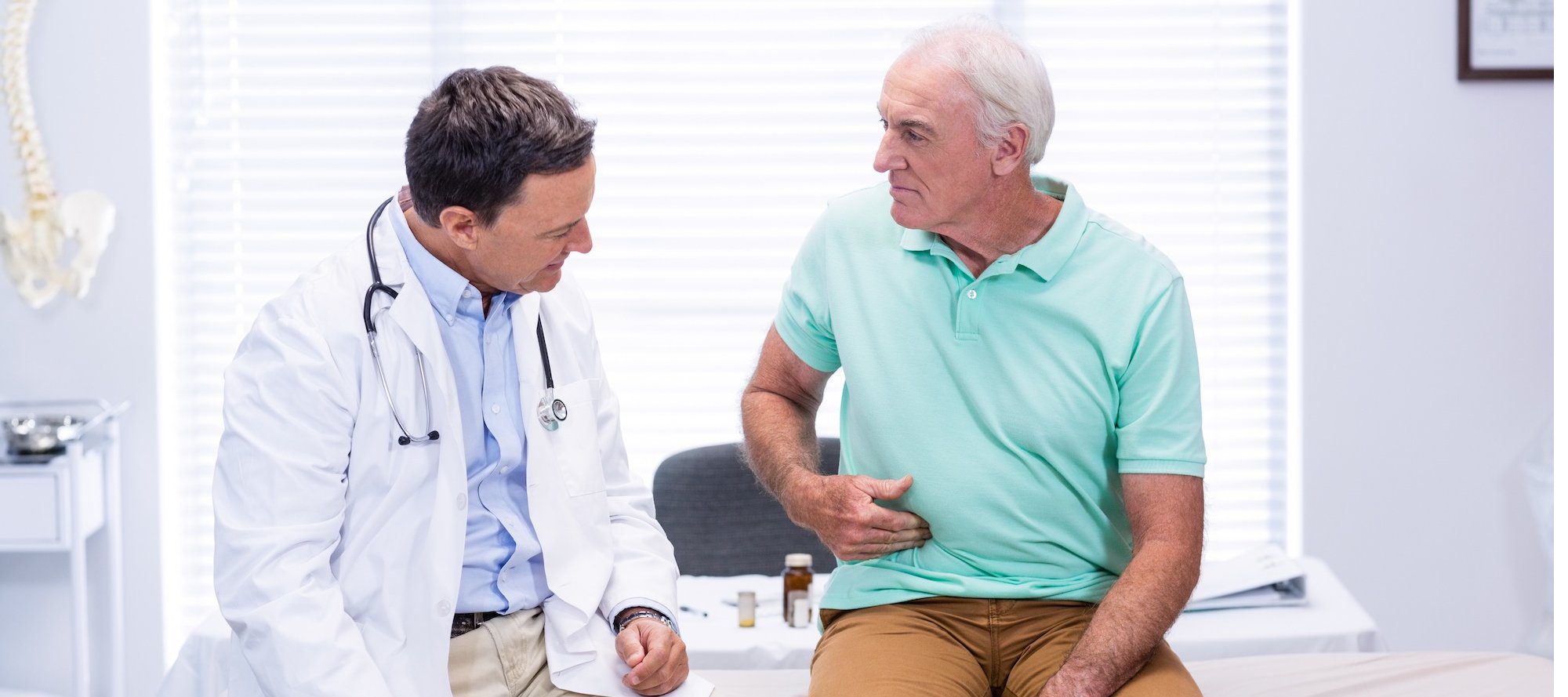Senior man showing stomach ache pain to doctor