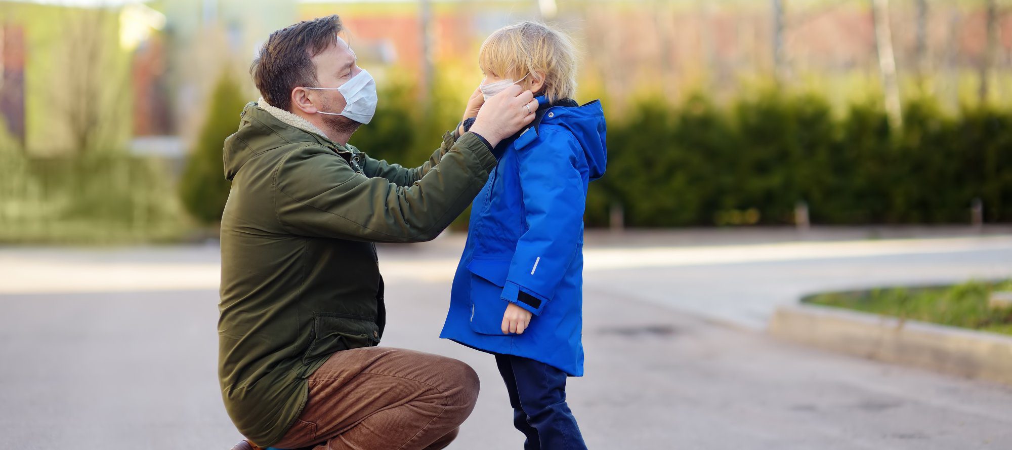 Mature man wearing a protective mask puts a face mask on a his son in airport