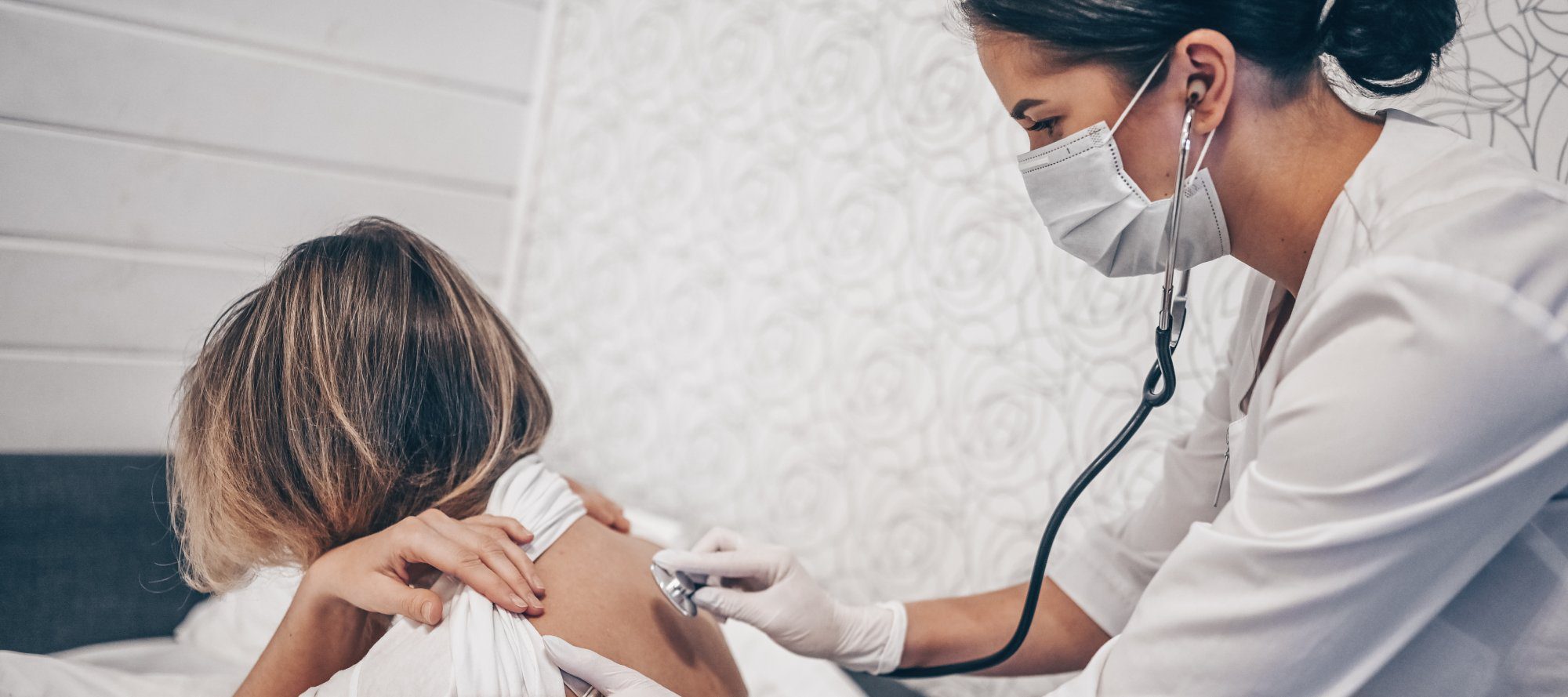Doctor nurse in protective face mask listening to breath with a stethoscope suspecting Coronavirus