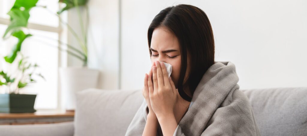 sick asian young woman sneezing into tissue paper while covered with a blanket