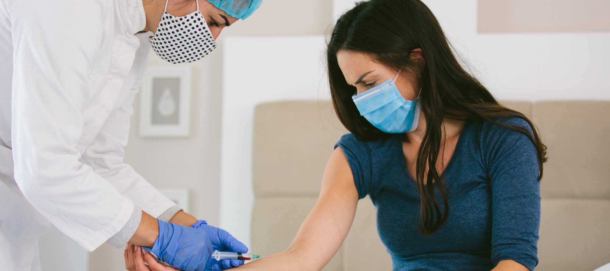 Nurse with mask protection drawing blood sample for Covid 19 test, from the arm of a female patient