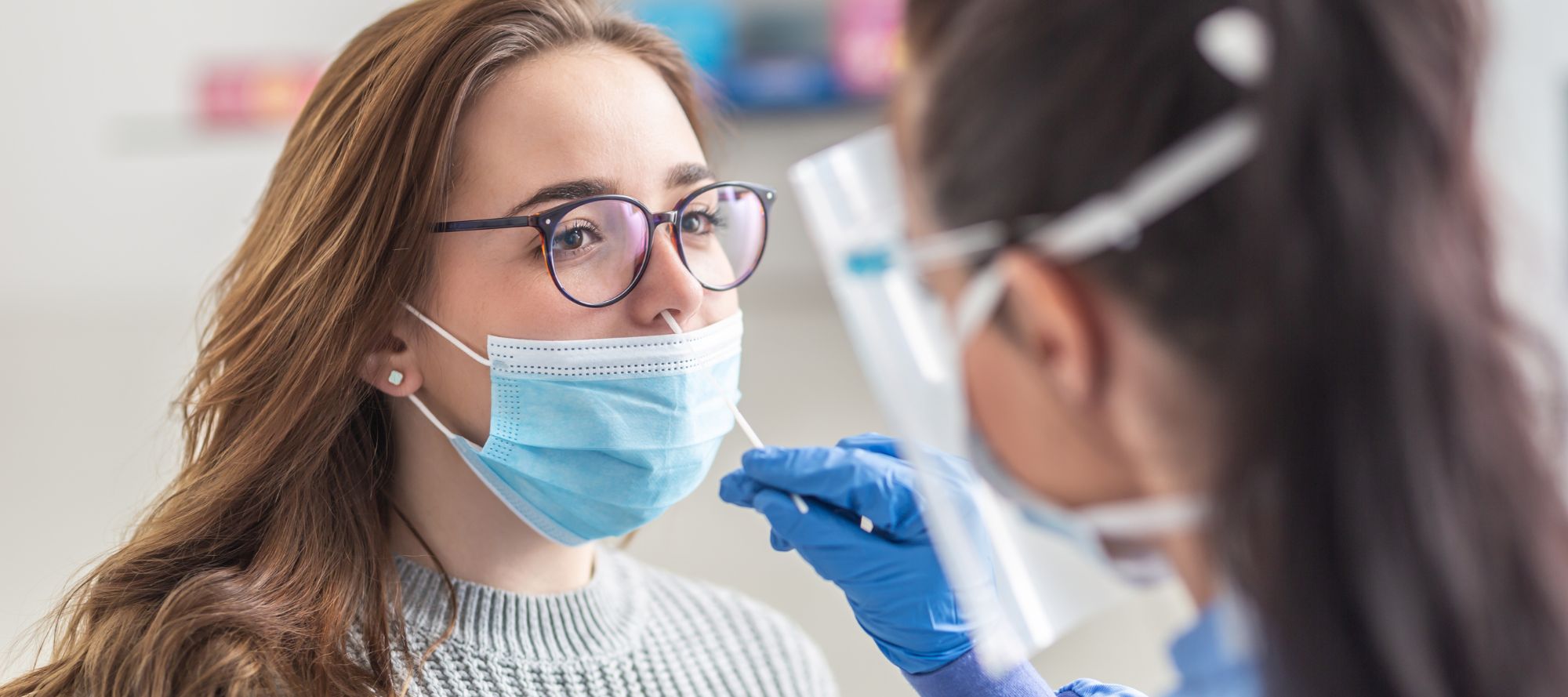 Female patient wearing mask over mouth is having sample taken from nose for a pcr test for Covid 19