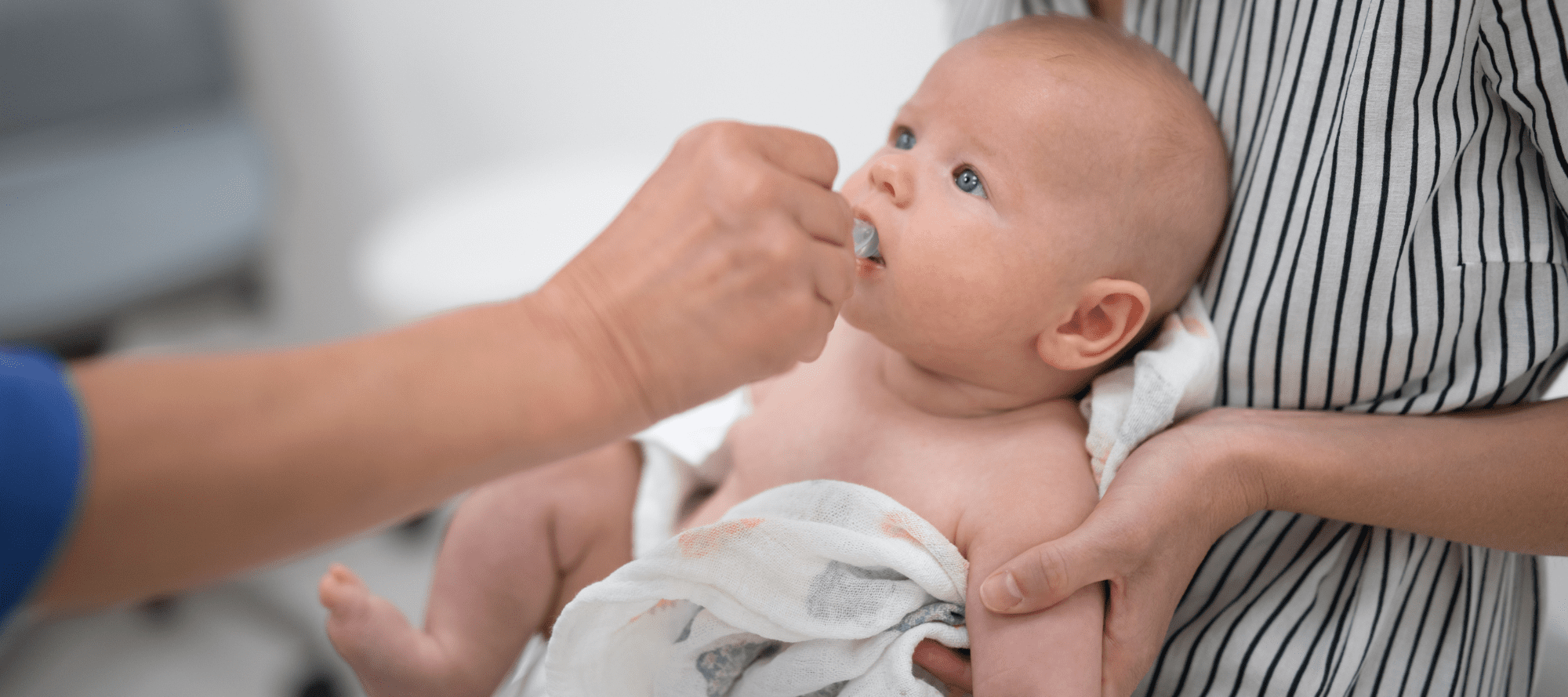 Pediatrician administering oral medication to baby in presence of his mother