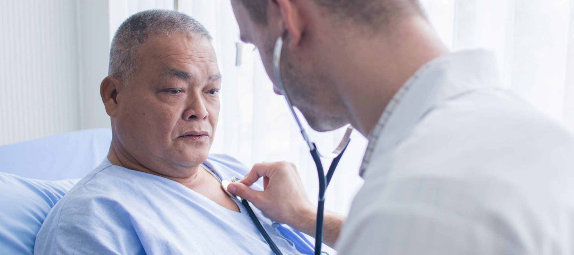 Doctor listening to adult male's heartbeat in hospital setting