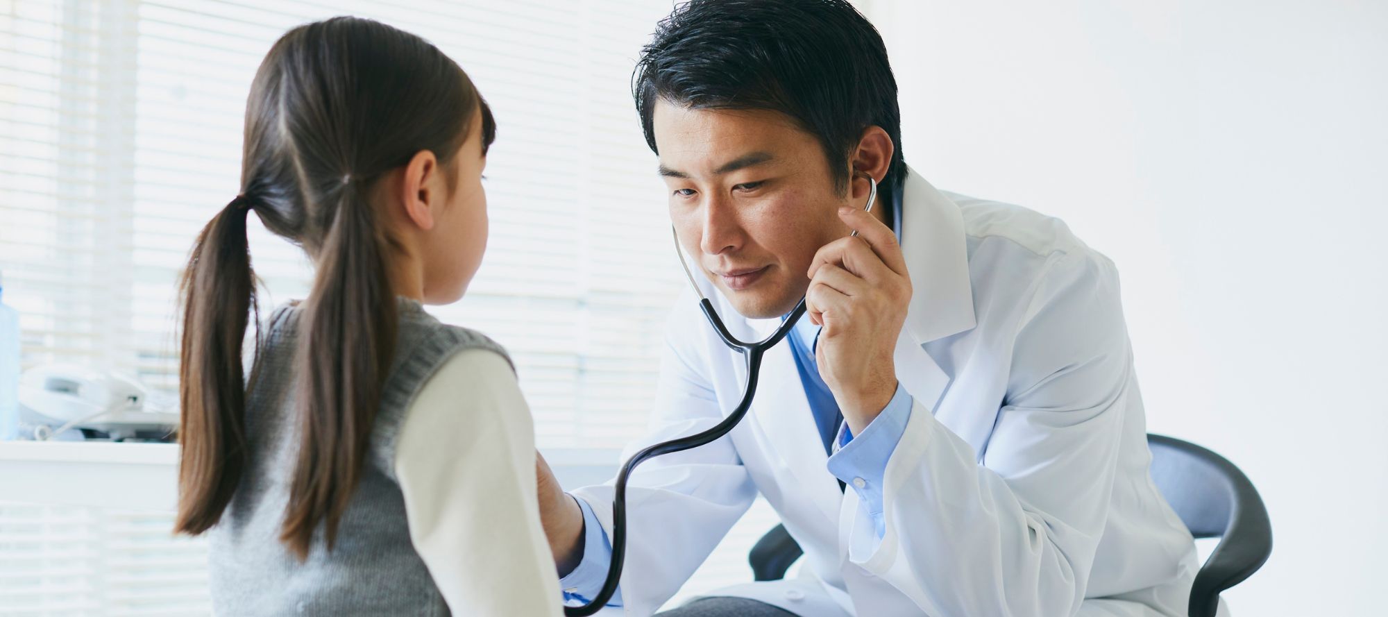 Young doctor holding stethoscope to child's heart during exam